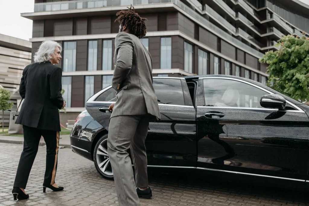 Chauffeur en costume ouvrant la portière d’une berline noire pour une cliente